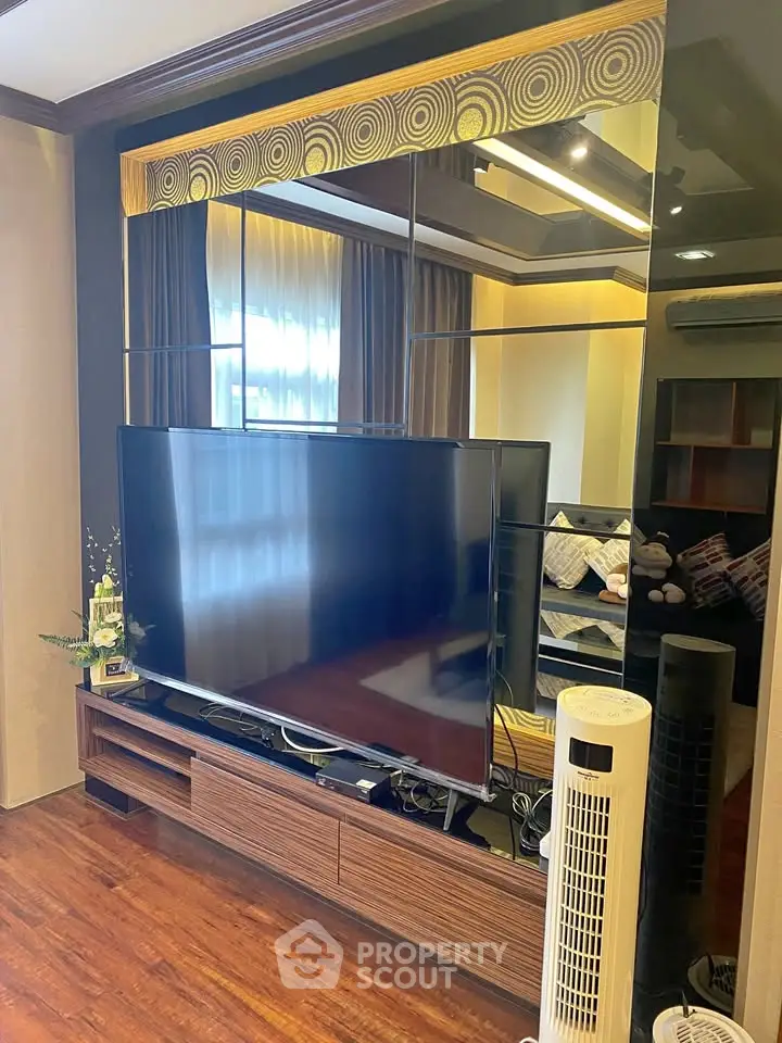 Modern living room with large TV and stylish decor, featuring wooden flooring and elegant curtains.