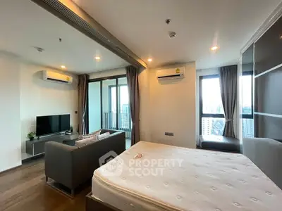 Modern studio apartment with large windows and city view, featuring a cozy living area and bed.