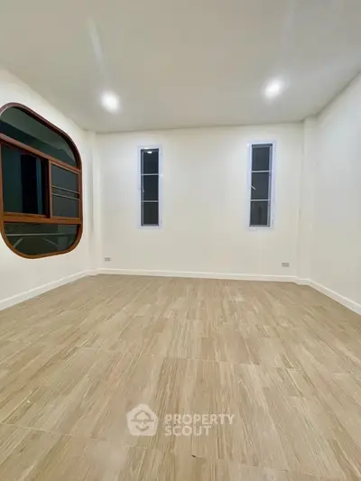 Spacious room with unique circular window and modern flooring, perfect for customization.