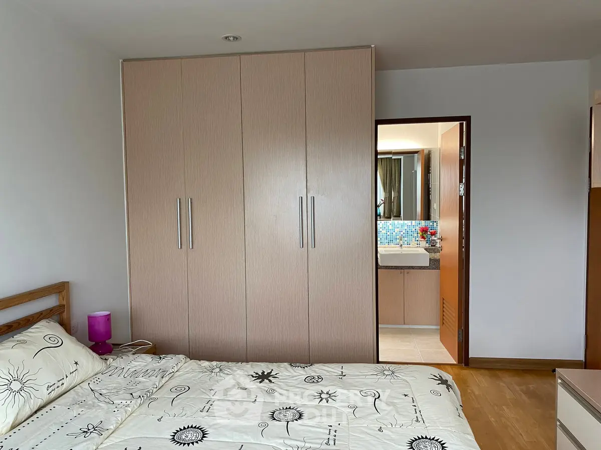 Cozy bedroom with wooden flooring and built-in wardrobe, adjacent to a modern bathroom.