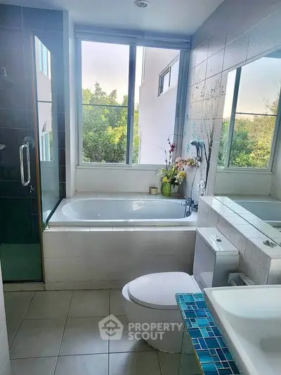 Bright bathroom with large window, bathtub, and modern fixtures offering serene garden views.