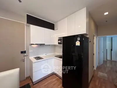 Modern kitchen with sleek black fridge and white cabinetry in compact layout.
