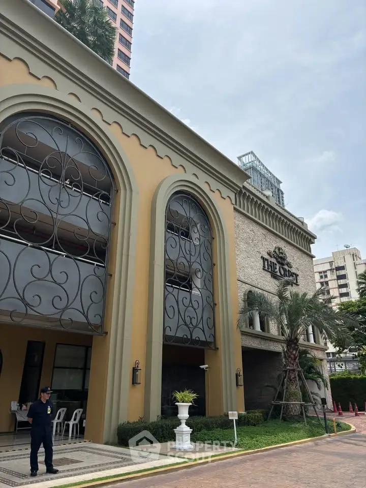 Elegant building facade with arched windows and lush landscaping in urban setting.