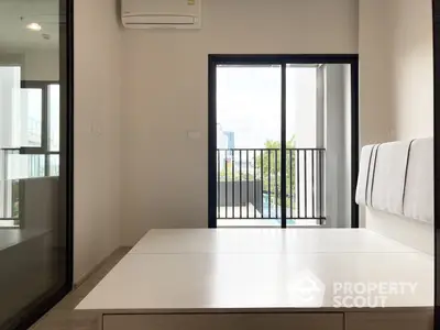 Bright and airy modern bedroom with large windows leading to a cozy balcony, offering a serene urban view and ample natural light.