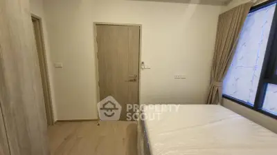 Cozy bedroom with wooden flooring and large window, featuring a comfortable bed and neutral decor.