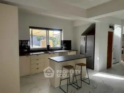 Modern kitchen with island and stools, featuring sleek appliances and ample natural light.