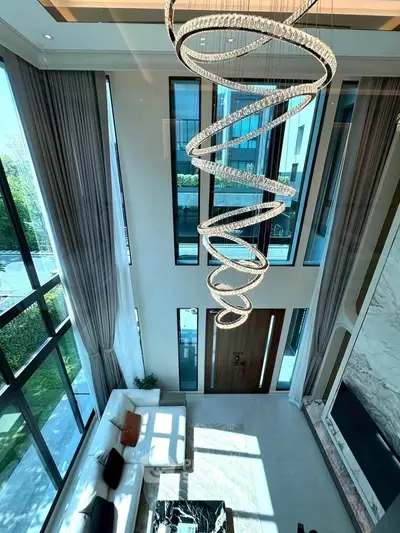 Luxurious high-ceiling living room with modern chandelier and large windows offering natural light.