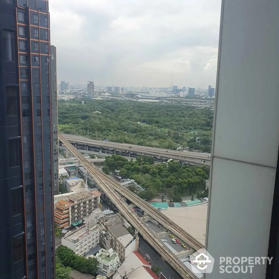 Stunning cityscape view from high-rise apartment overlooking lush greenery and urban skyline.