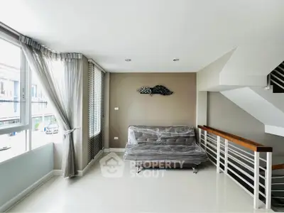 Modern living room with large windows and staircase, featuring a wrapped sofa and elegant decor.