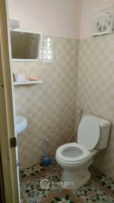Compact bathroom with tiled walls and floor, featuring a toilet and small sink.