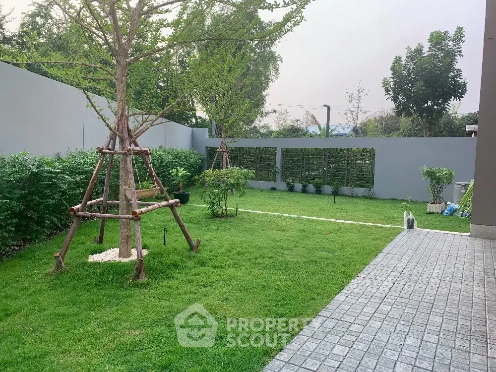 Spacious green garden with lush trees and paved walkway in modern residential property.