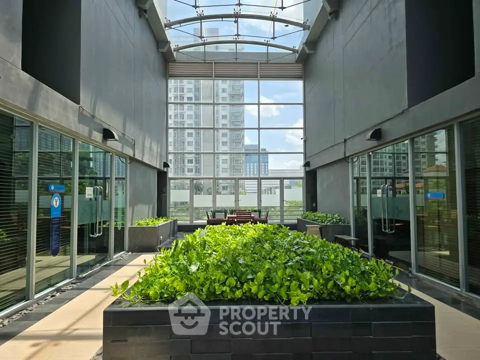 Modern building entrance with glass ceiling and lush greenery, offering a welcoming and stylish ambiance.