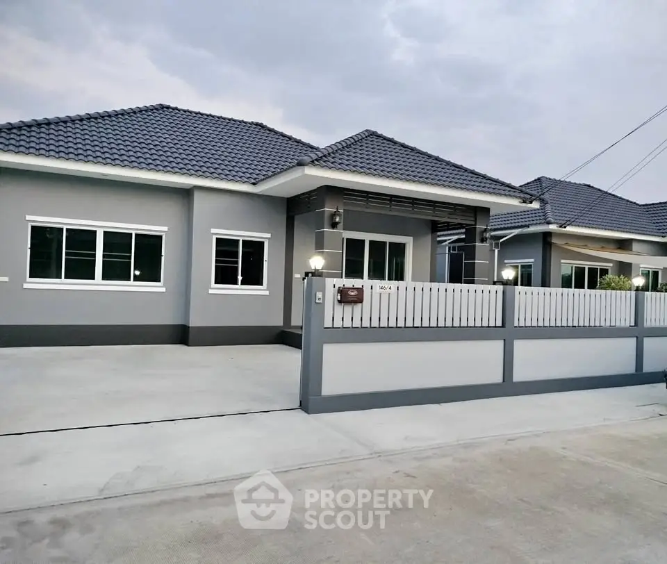 Modern single-story house with gray exterior and tiled roof, featuring a spacious driveway and fenced yard.