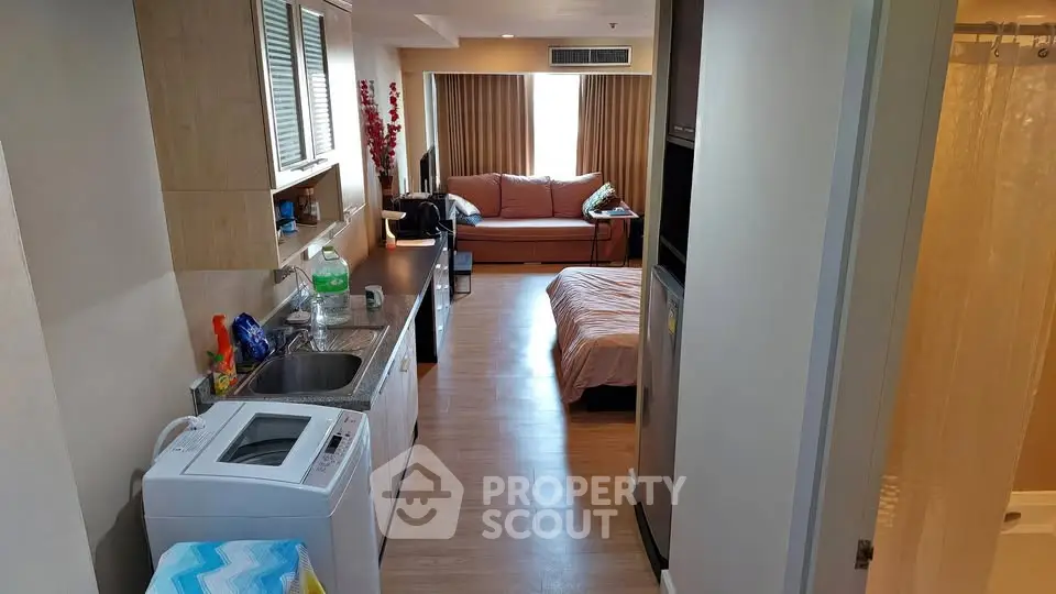 Cozy studio apartment with open kitchen and living area, featuring a washing machine and comfortable furnishings.