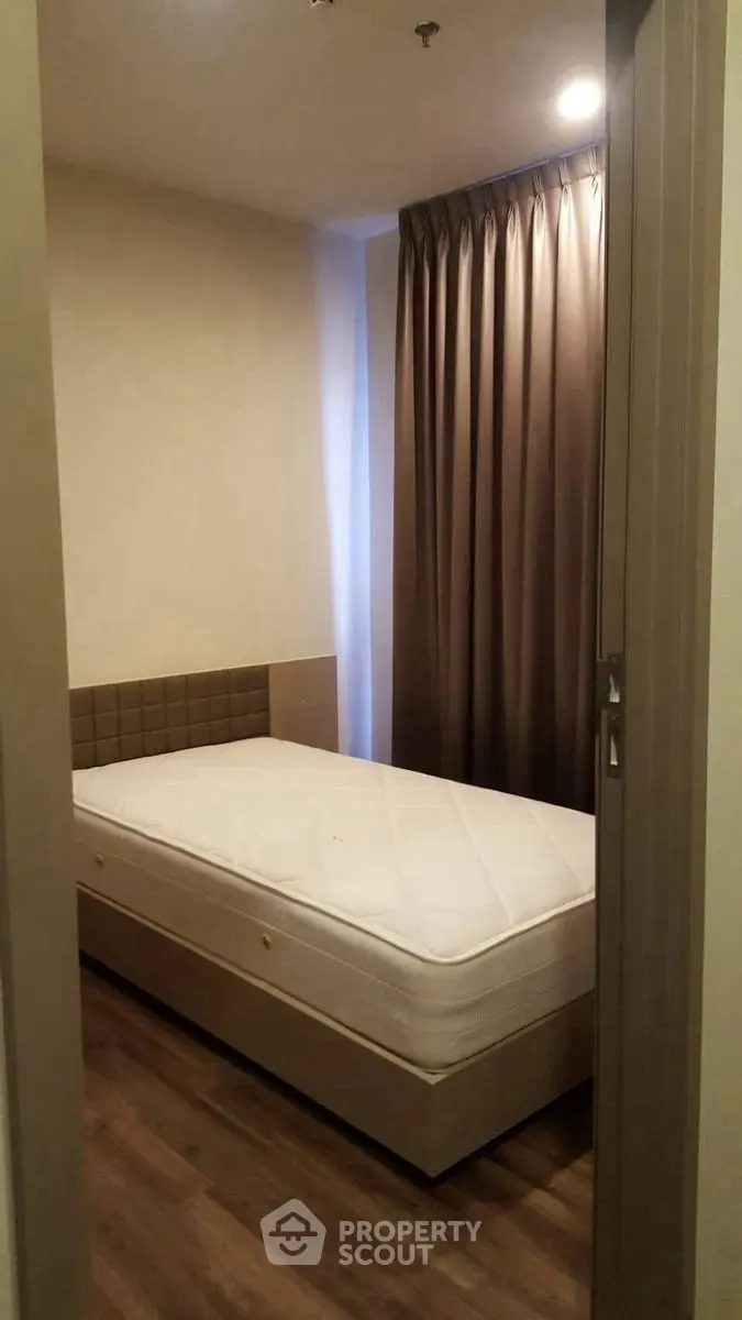 Cozy single bedroom with wooden flooring and elegant curtains, perfect for a minimalist lifestyle.
