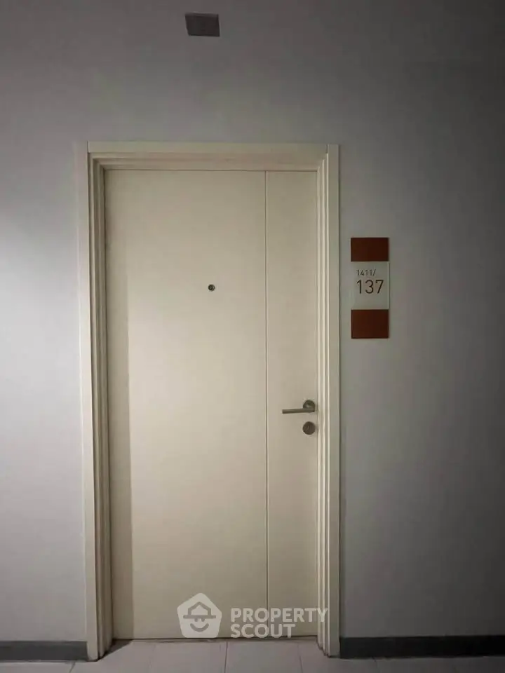 Modern apartment entrance with sleek white door and room number 137 on the wall.