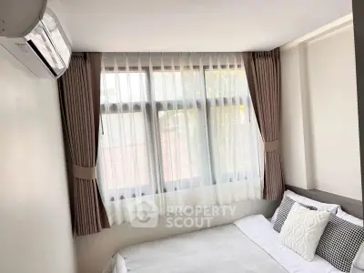 Cozy bedroom with large window and elegant curtains, featuring a comfortable bed and air conditioning unit.