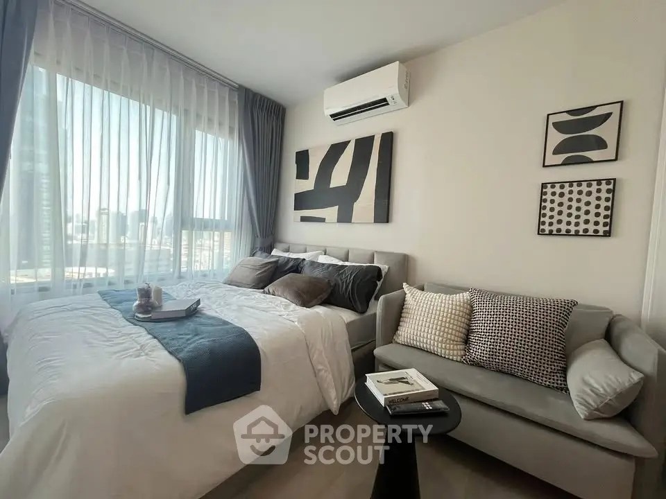 Modern bedroom with stylish decor, featuring a cozy bed, chic sofa, and large window with city view.