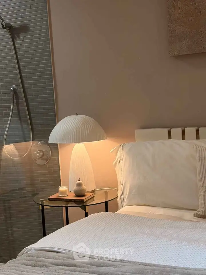 Cozy bedroom with elegant bedside lamp and modern shower area, perfect for relaxation.