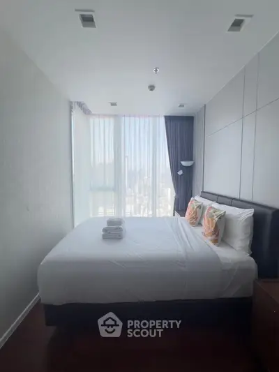 Modern bedroom with large window and city view, featuring elegant decor and cozy bedding.