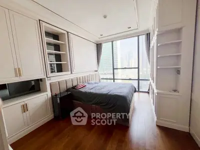 Luxurious bedroom with city view, elegant built-in storage, and hardwood flooring.