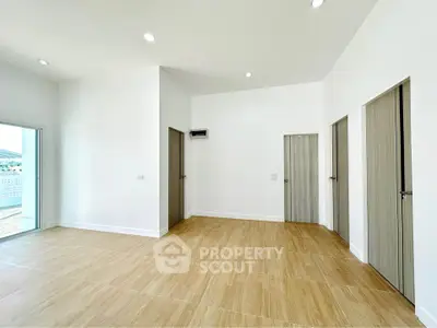 Spacious modern room with wooden flooring and multiple doors, ideal for versatile living space.