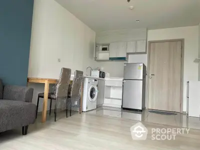 Modern apartment interior with compact kitchen and dining area, featuring washing machine and fridge.