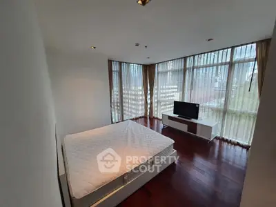 Spacious bedroom with large windows and city view, featuring hardwood floors and modern furnishings.