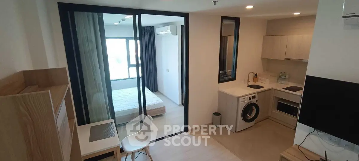 Modern studio apartment with open kitchen and bedroom, featuring a washing machine and sleek design.