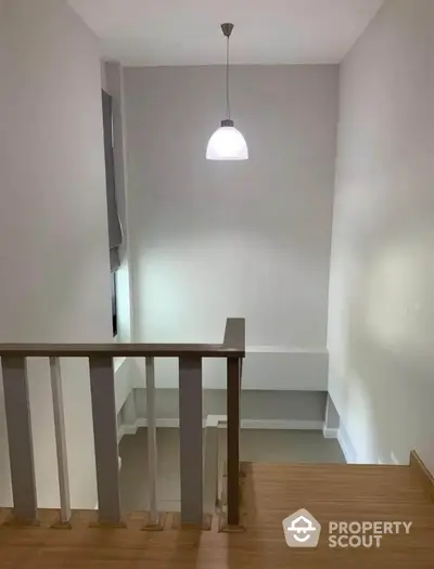 Modern staircase with wooden steps and sleek railing under a minimalist pendant light.