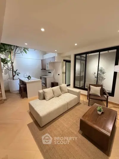 Modern living room with open kitchen, featuring stylish furniture and elegant lighting.