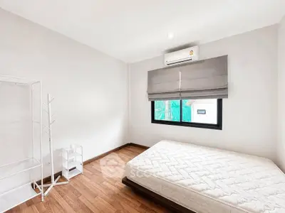 Spacious bedroom with wooden flooring and natural light, featuring a minimalist design and air conditioning.