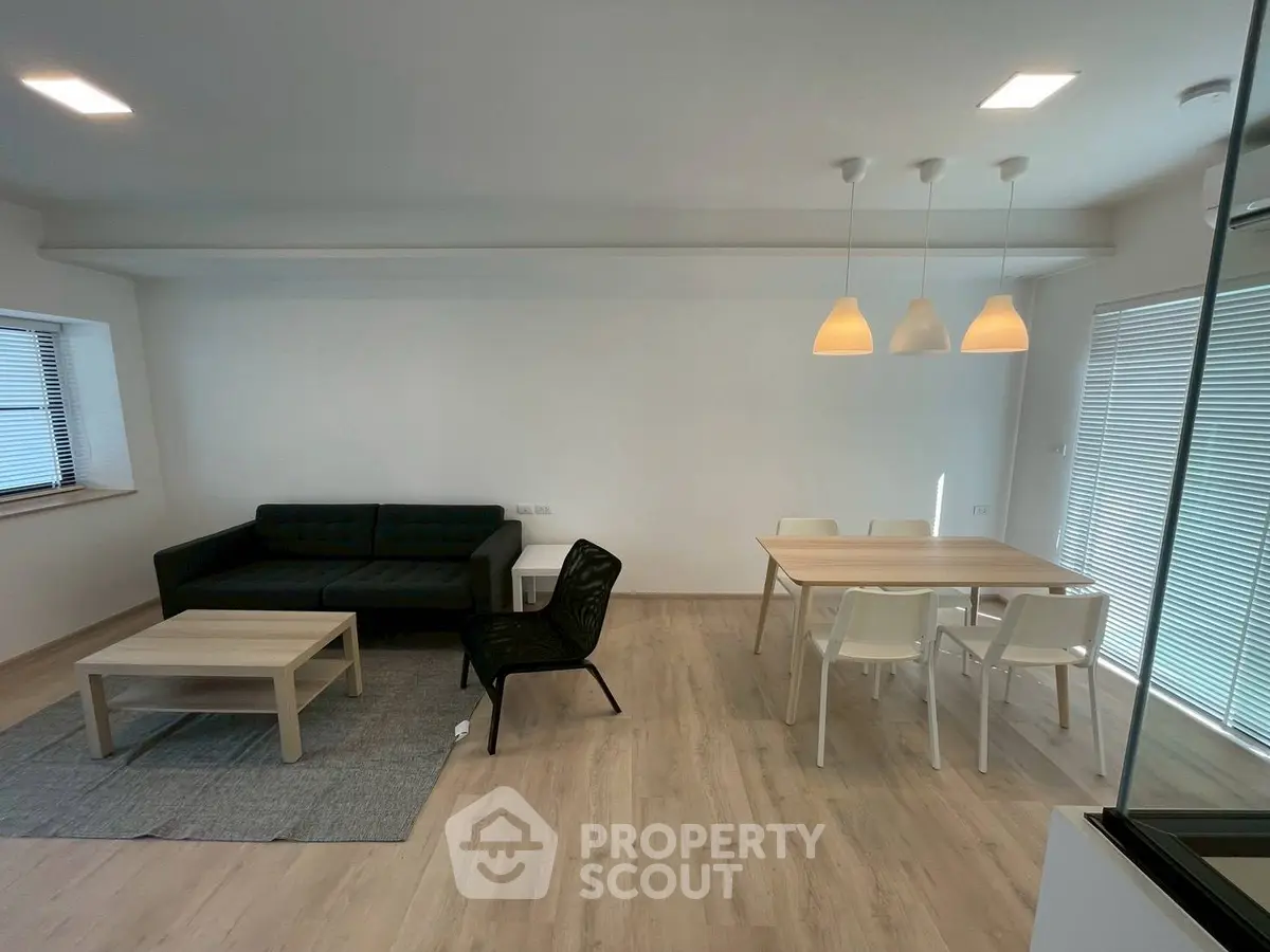 Modern living room with sleek furniture and dining area, featuring minimalist design and ample natural light.