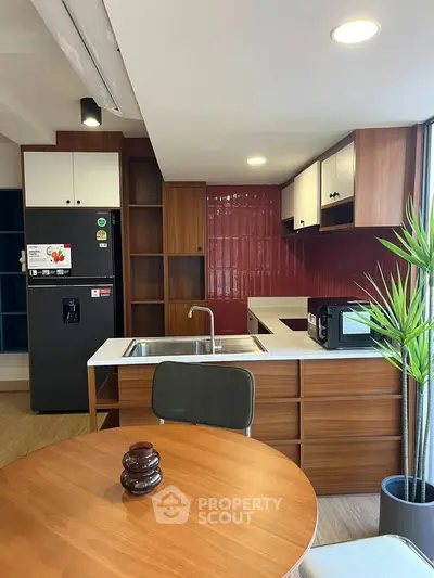Modern kitchen with sleek wooden cabinets and red backsplash, featuring a fridge and microwave.