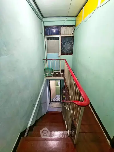 Charming vintage staircase with wooden steps and vibrant railing in a cozy home.