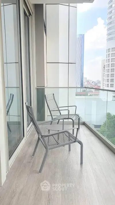 Modern balcony with glass railing and city view, featuring two sleek chairs on wooden flooring.