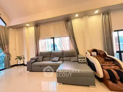 Spacious living room with modern sofa and massage chair, elegant curtains and natural light.