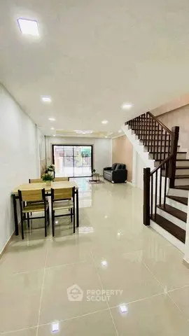Spacious modern living room with dining area and staircase, featuring sleek tile flooring and bright lighting.