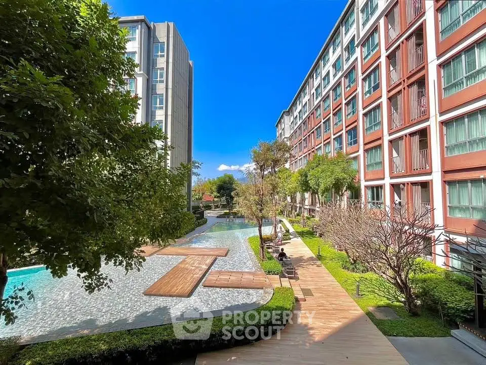 Modern apartment complex with lush garden and serene pool area under clear blue sky.