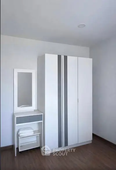 Modern minimalist bedroom with sleek wardrobe and vanity set on wooden flooring.