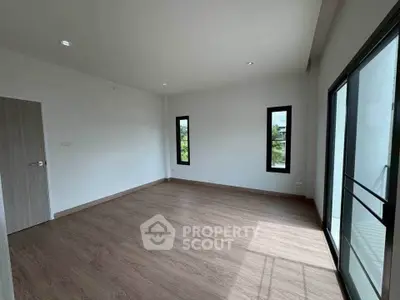 Spacious empty room with wooden flooring and large windows offering natural light.
