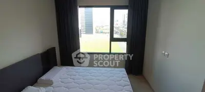 Modern bedroom with large window offering city view, featuring a comfortable bed and elegant curtains.