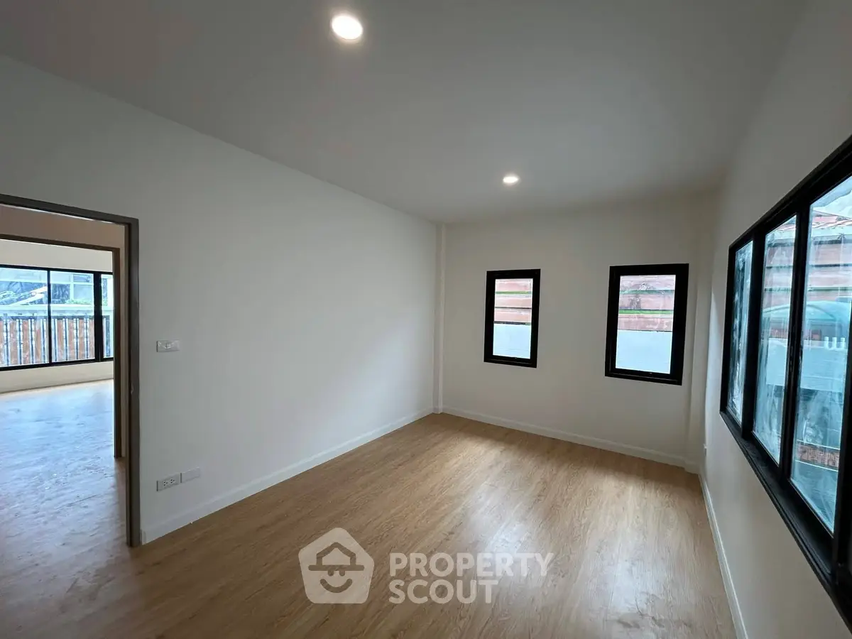 Spacious empty room with wooden flooring and large windows in modern apartment.