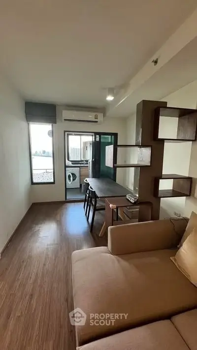 Modern living room with open balcony and washing machine, featuring sleek wooden flooring and contemporary furniture.