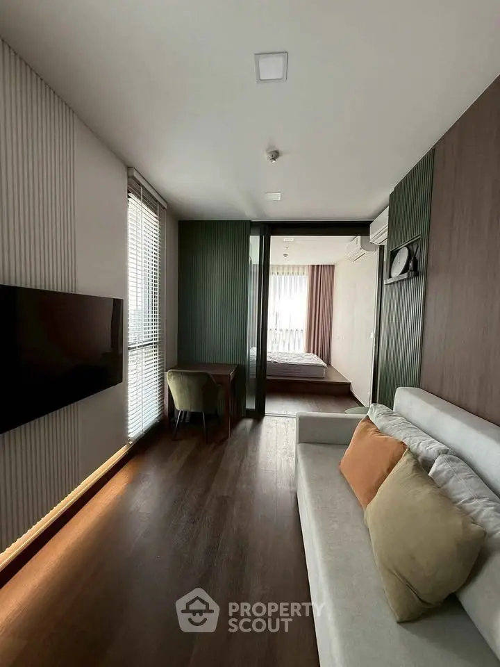 Modern living room with sleek design and natural light leading to a cozy bedroom.