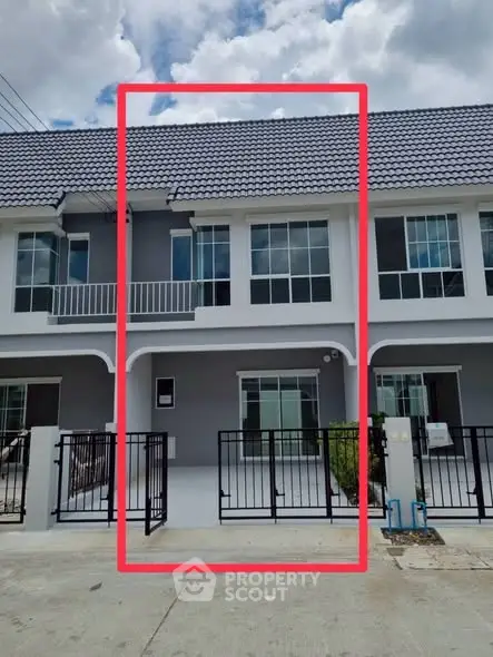 Modern townhouse exterior with gated entrance and balcony under a cloudy sky.