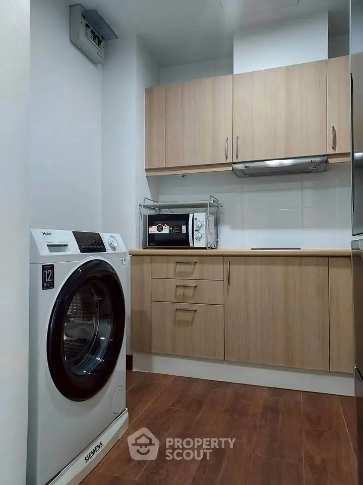 Modern kitchen with wooden cabinets, washing machine, and microwave, featuring sleek design and efficient layout.