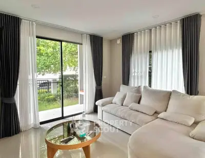 Spacious living room with large windows and modern furniture, offering a serene garden view.