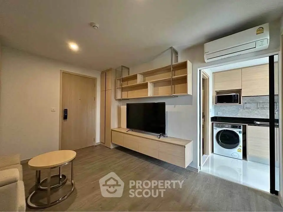 Modern living room with built-in TV unit and adjacent kitchen featuring appliances.