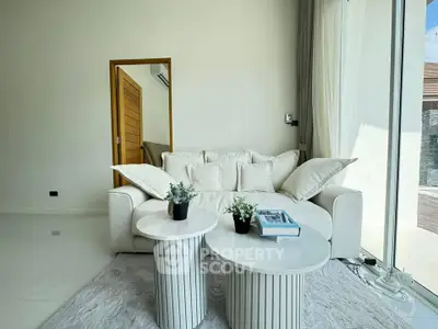 Modern living room with white sofa, elegant coffee tables, and large windows for natural light.